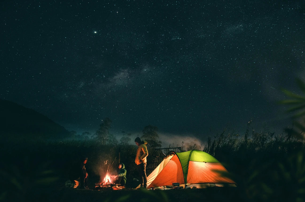 Kampeerders by 'n tent onder 'n sterrehemel