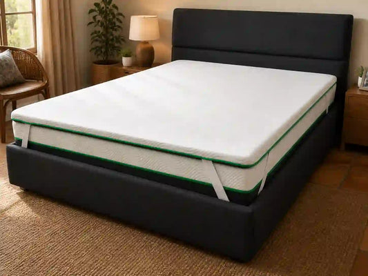 Wit matras topper met groen afwerking op ’n donker gestoffeerde bed in ’n warm slaapkamer